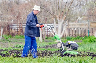 Bir adam bir bahar bahçesinde ekiciyle toprağı sürüyor..