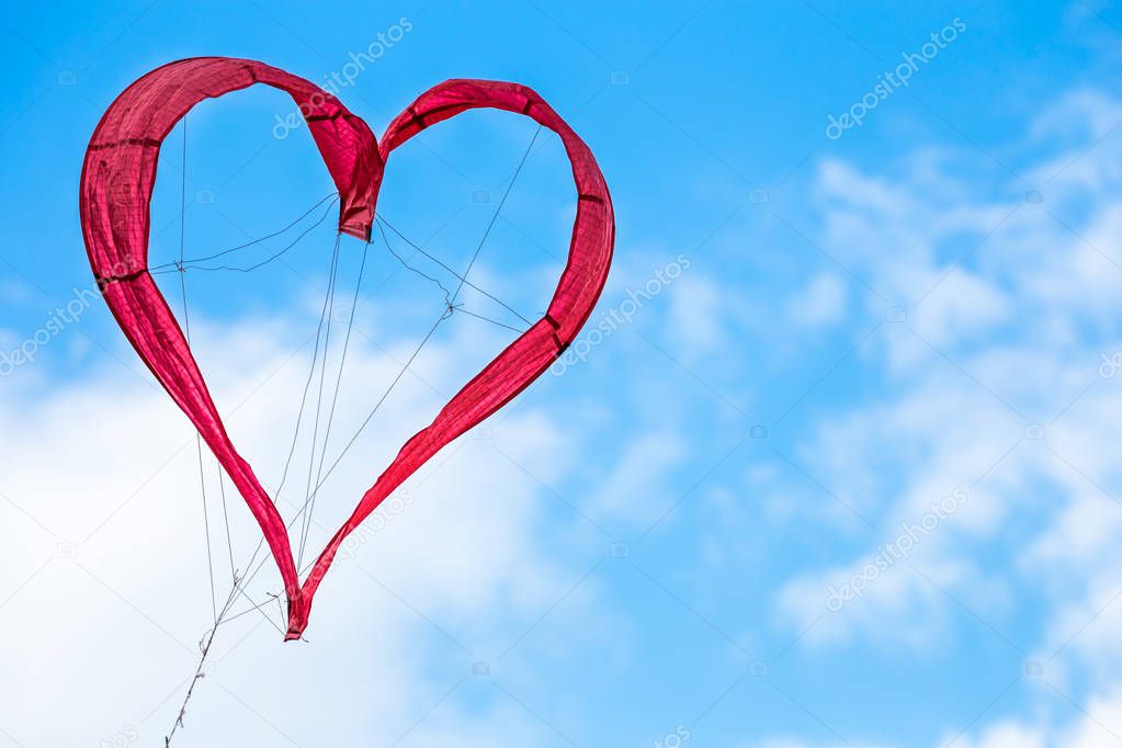 White clouds on blue sky with red heart shaped kite