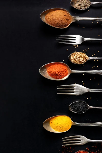 Kryddor på skedar på svart bakgrund, ovanifrån — Stockfoto