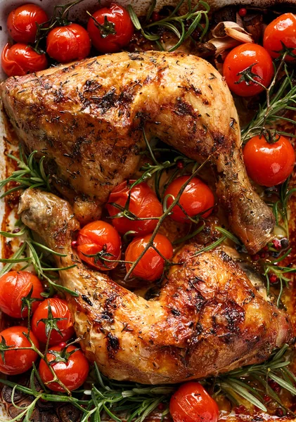 Baked chicken quarter with cherry tomatoes and rosemary in a casserole dish on wooden table