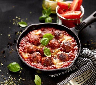 Meatballs in tomato sauce with addition cheese and fresh basil on iron pan clipart