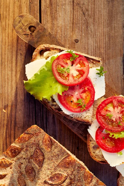 Вегетаріанські бутерброди з додаванням сиру, помідорів і салату на сільському дерев'яному столі — стокове фото