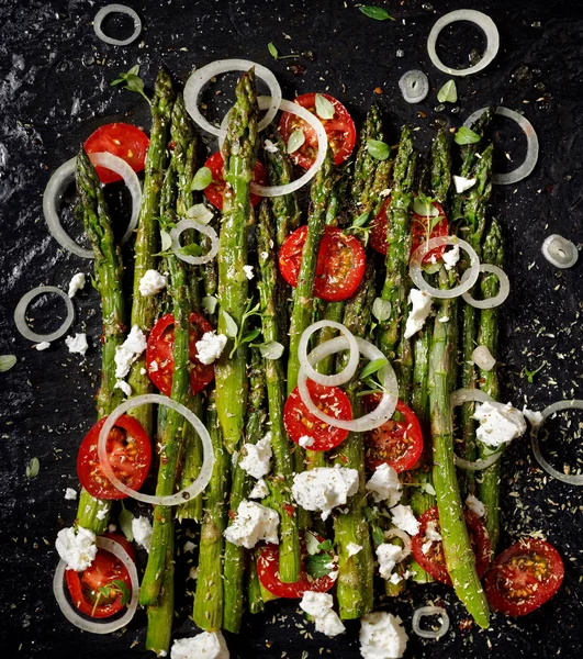 Salade met gegrilde groene asperges, cherry tomaten, ui en feta kaas op zwarte achtergrond, bovenaanzicht — Stockfoto