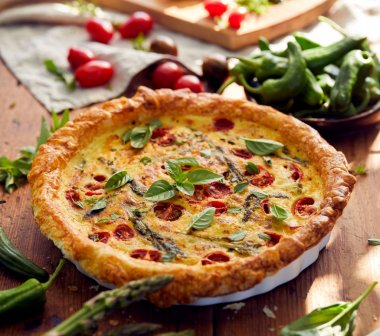 Vejetaryen quiche kiraz domates ve rustik ahşap bir masa üzerinde yeşil kuşkonmaz ile