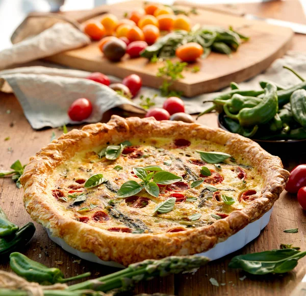 Quiche com tomates cereja e espargos verdes em uma mesa de madeira rústica — Fotografia de Stock