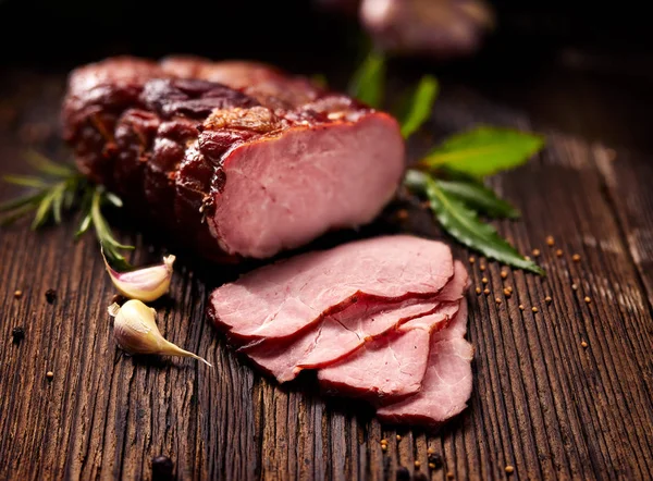 Geräucherter Schinken in Scheiben geschnitten auf einem rustikalen Holztisch mit frischen aromatischen Kräutern — Stockfoto