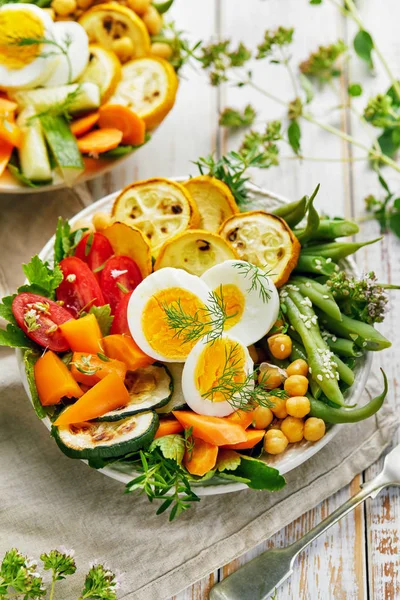 Вегетаріанський салат із зеленою квасолею, кабачками на грилі, помідорами, нутом, морквою та вареними яйцями, посипаними свіжими травами у керамічній мисці. Концепція здорового харчування — стокове фото