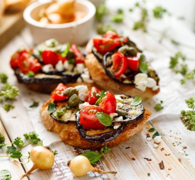 Bruschetta ızgara patlıcan, domates, beyaz peynir, Kapari ve ahşap bir masa üzerinde taze aromatik otlar. Lezzetli Akdeniz meze