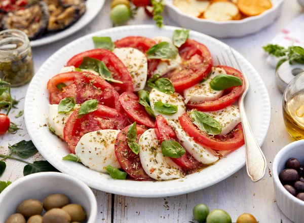 Dilimlenmiş taze domateslerden yapılmış Caprese salatası, mozzarella peyniri ve fesleğen ahşap bir masada beyaz bir tabakta servis edilir. Geleneksel İtalyan yemeği. — Stok fotoğraf