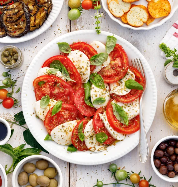Caprese salát z nakrájených čerstvých rajčat, mozzarella sýra a bazalky podávané na bílém talíři na dřevěném stolku.Tradiční italské jídlo — Stock fotografie