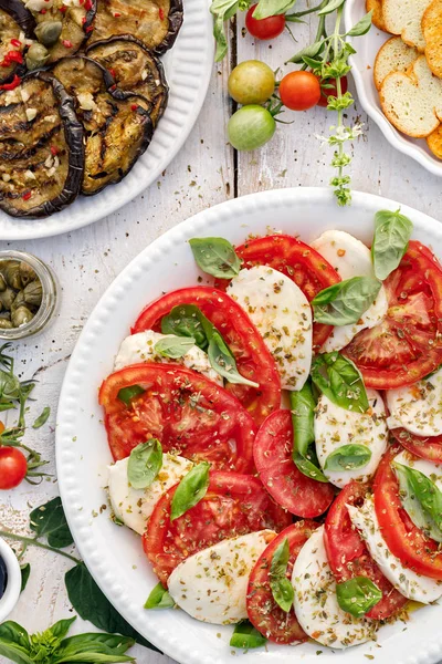 Salată de caprese din roșii proaspete feliate, brânză mozzarella și busuioc servite pe o farfurie albă pe o masă de lemn.Mâncare tradițională italiană — Fotografie, imagine de stoc