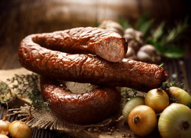 Smoked  sausage on a wooden rustic table with addition of fresh aromatic herbs and spices, natural product from organic farm, produced by traditional methods clipart