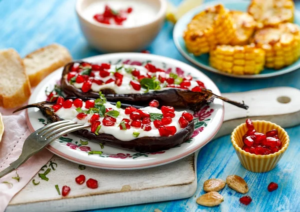 Grillad aubergine med yoghurtsås, granatäpplekärnor och färska örter på en keramisk platta. Begreppet läcker och hälsosam vegetarisk måltid — Stockfoto