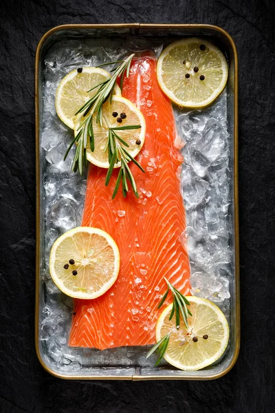 Fresh raw fish fillet on ice with lemon slices, rosemary, salt and peppercorns, top view — Stock Photo, Image