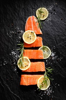 Siyah taş zemin üzerine limon dilimleri, biberiye, tuz ve biber ile porsiyon taze çiğ balık fileto kesilmiş