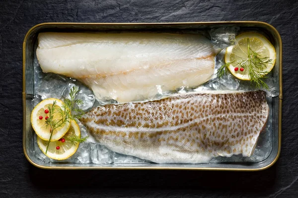 Fresh fish, cod fillets on ice with lemon slices, dill and red peppercorns, top view, horizontal setting — Stock Photo, Image