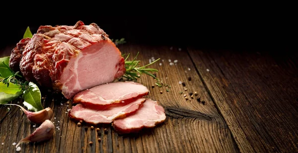 Smoked gammon on a wooden rustic table with addition of fresh aromatic herbs, top view.  Natural product from organic farm, produced by traditional methods