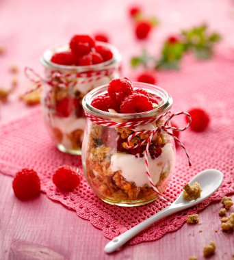Granola taze Ahududu ve ahşap bir pembe tablo bir cam kavanoza doğal yoğurt ile. Lezzetli kahvaltı ya da tatlı. Sağlıklı beslenme kavramı