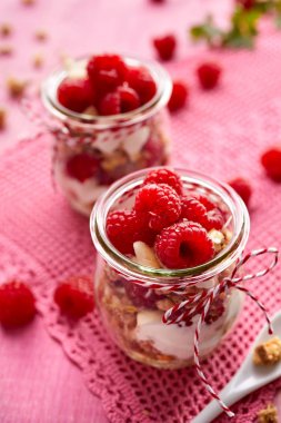 Granola taze Ahududu ve ahşap bir pembe tablo bir cam kavanoza doğal yoğurt ile. Lezzetli kahvaltı ya da tatlı. Sağlıklı beslenme kavramı