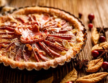 Elmalı tart, kırmızı elmalı tart, tarçın, badem gevreği ve bal, ahşap bir arka planda pudra şekeri serpiştirilmiş, yakın plan. Lezzetli bir ev yapımı tatlı.