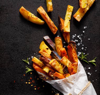 Patates kızartması, farklı türlerden fırınlanmış patates kızartması ve siyah arka planda siyah bir çantanın içinde otlar ve baharatlar serpiştirilmiş, yakın plan,.
