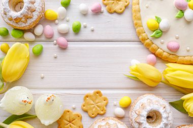 Badem ezmesi yumurtalı Paskalya arkaplanı, mazurek pastası, maya keki ve bahar çiçekleri beyaz ahşap arka planda, üst manzara, kopyalama alanı.