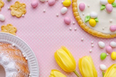 Badem ezmesi yumurtalı Paskalya arkaplanı, paskalya pastası ve bahar çiçekleri pembe arka planda beyaz noktalı üst görünümde, boşluğu kopyala