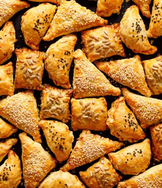 İçinde tohumlar serpiştirilmiş çeşitli dolgularla puf böreği. Fransız hamur işi mantarlar, siyah arka planda ıspanak ve peynir, üst manzara, yakın plan. Lezzetli aperatifler, parmak yemekleri, atıştırmalıklar..
