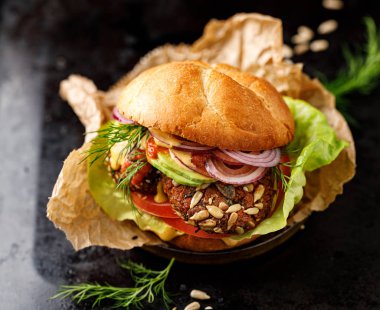 Vejetaryen burger, havuç ve darı burger, havuç ve darı pirzolası ile birlikte domates, avokado dilimleri, kırmızı soğan, marul ve siyah arka planda taze bitkiler. Sağlıklı beslenme