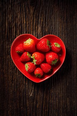 Kırsal bir masada kırmızı kalp şeklinde bir tabakta taze çilekler. Lezzetli bir Sevgililer Günü tatlısı