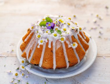 Paskalya maya keki (Babka) kremayla kaplı ve beyaz ahşap bir masada beyaz bir tabakta yenilebilir çiçeklerle süslenmiş. Polonya 'da geleneksel Paskalya pastası