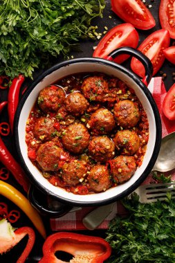 Meatballs in tomato sauce with the addition of aromatic herbs in an enamel dish top view clipart
