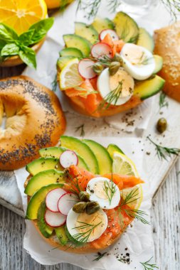 Somon füme bagel sandviç, avokado haşlanmış yumurta turp limon ve beyaz ahşap bir masada taze dereotu, üst manzara. Lezzetli ve sağlıklı kahvaltı.