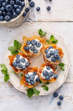 Mascarpone peynirli Phyllo bardakları beyaz tepsi manzarasında üzerine pudra şekeri serpiştirilmiş taze yaban mersinleri serpiştirilmiş. Lezzetli fileto pasta tatlısı