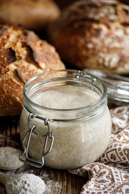 Ahşap bir masada ekmek pişirmek için aktif çavdar ekmeği içeren bir kavanoz.
