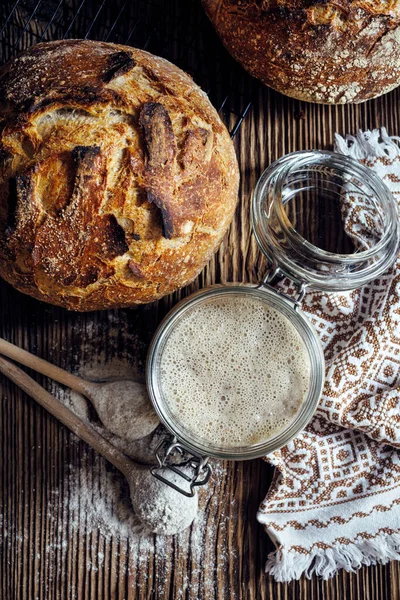 Rye sourdough starter in glass jar and homemade sourdough bread on a rustic wooden table, top view