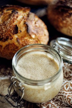 Ahşap bir masada ekmek pişirmek için aktif çavdar ekmeği içeren bir kavanoz.