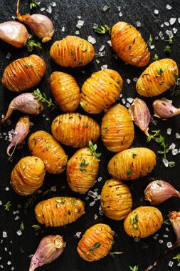 Fırında patates, sarımsaklı hasselback ve siyah arka planda kekik. 
