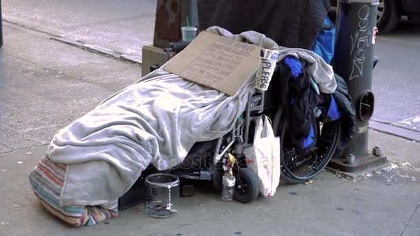 People passing by homeless man in wheelchair on street - snowing at night in winter in NYC. Homelessness is an epidemic in major US cities. — Stock Video