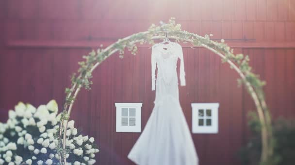 Vestido de noiva elegante pendurado no arco decorado com flores à luz do dia — Vídeo de Stock