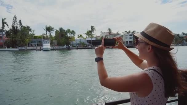 Junges Mädchen auf dem Schiff macht Foto mit dem Handy von den luxuriösen Villen auf Sterneninsel, sonnigen Inselstrand, Miami — Stockvideo