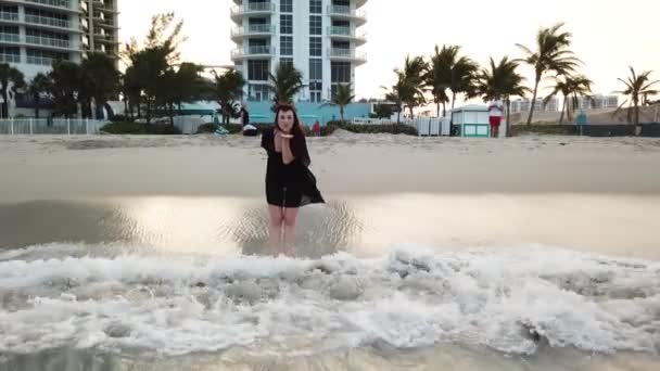 Kvinnan i svart klänning står i vågiga vattnet i havet och skickar luft kiss nära miami resort på sunny isles beach — Stockvideo