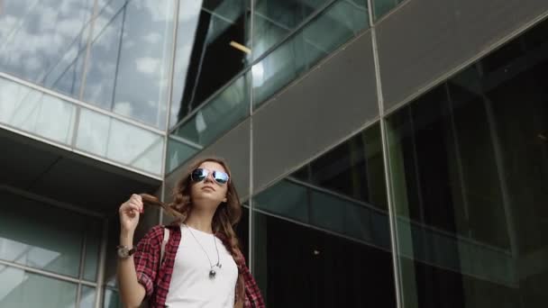 Marzyli dziewczyna z okulary stojący w pobliżu nowoczesnego budynku — Wideo stockowe