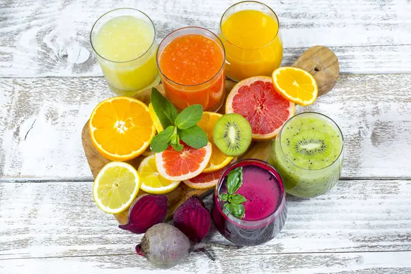 Tahta arka planda cam şişelerdeki meyve ve sebzelerden taze detoks sıvıları.