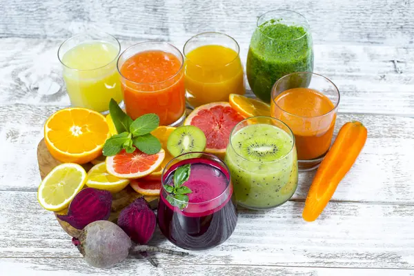 Tahta arka planda cam şişelerdeki meyve ve sebzelerden taze detoks sıvıları.