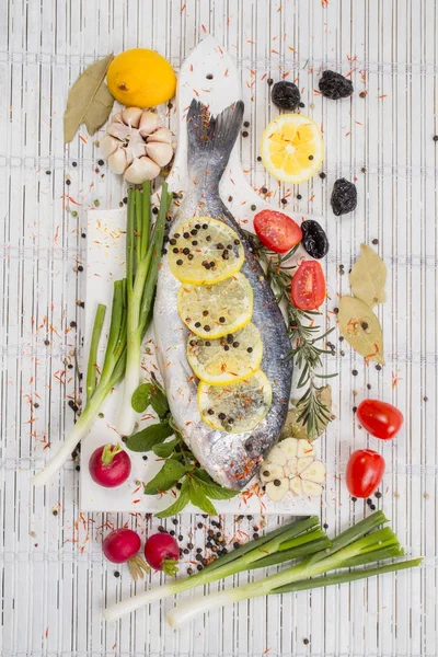 Sea bass with vegetables and spices on white wooden background — Stock Photo, Image