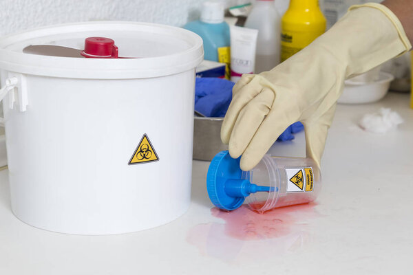 person cleaning a waste container labeled as biological risk