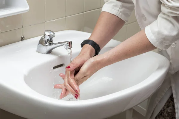 Beyaz bir lavabo su akışı altında elleri olan bir kişinin görünümü