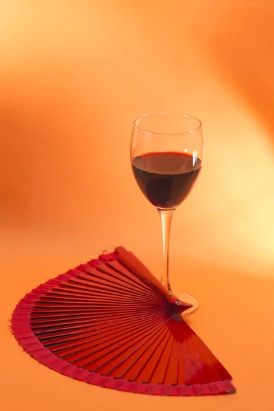Стакан красного вина рядом с красным вентилятором страсти, оранжевый фон — стоковое фото