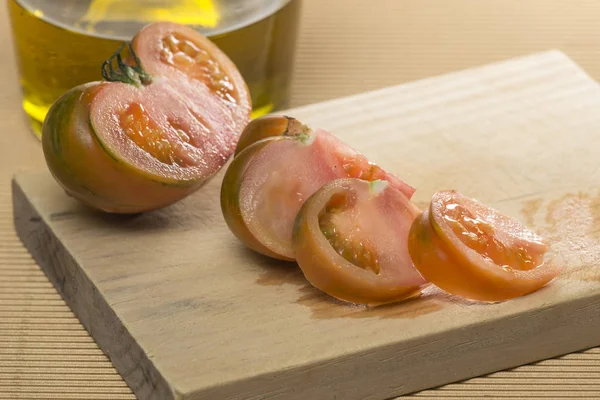Pomidor krojony na drewnianej desce, obok porronu oleju — Zdjęcie stockowe